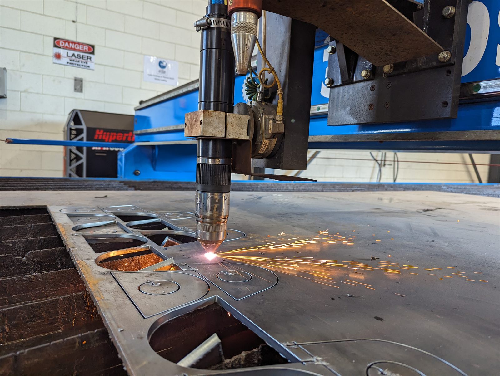 Close-up of a plasma cutting torch cutting steel plate, throwing a wide shower of hot orange sparks across the cutting bed.