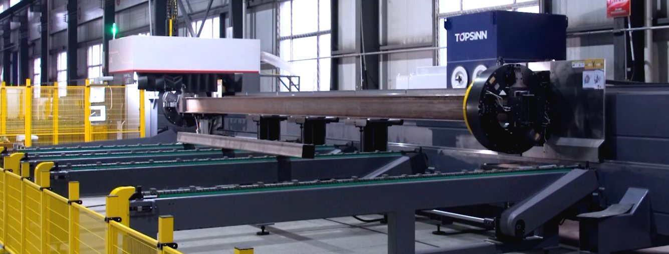 A tube laser cutting machine with a length of steel section loaded through the chuck, and a Topsinn dust collector positioned behind the cutting enclosure.